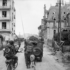 A_jeep_and_other_vehicles_and_troops_passing_through_La_Breche_as_they_move_inland_from_Sword_Beach,_Normandy,_6_June_1944._B5036