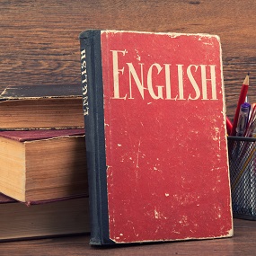 Books piled on top of one another next to a pen pot with a red book in front titled `English'.