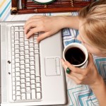 Student at home working on a computer and drinking coffee