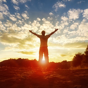 person with arms outstretched and sun setting in the bankground